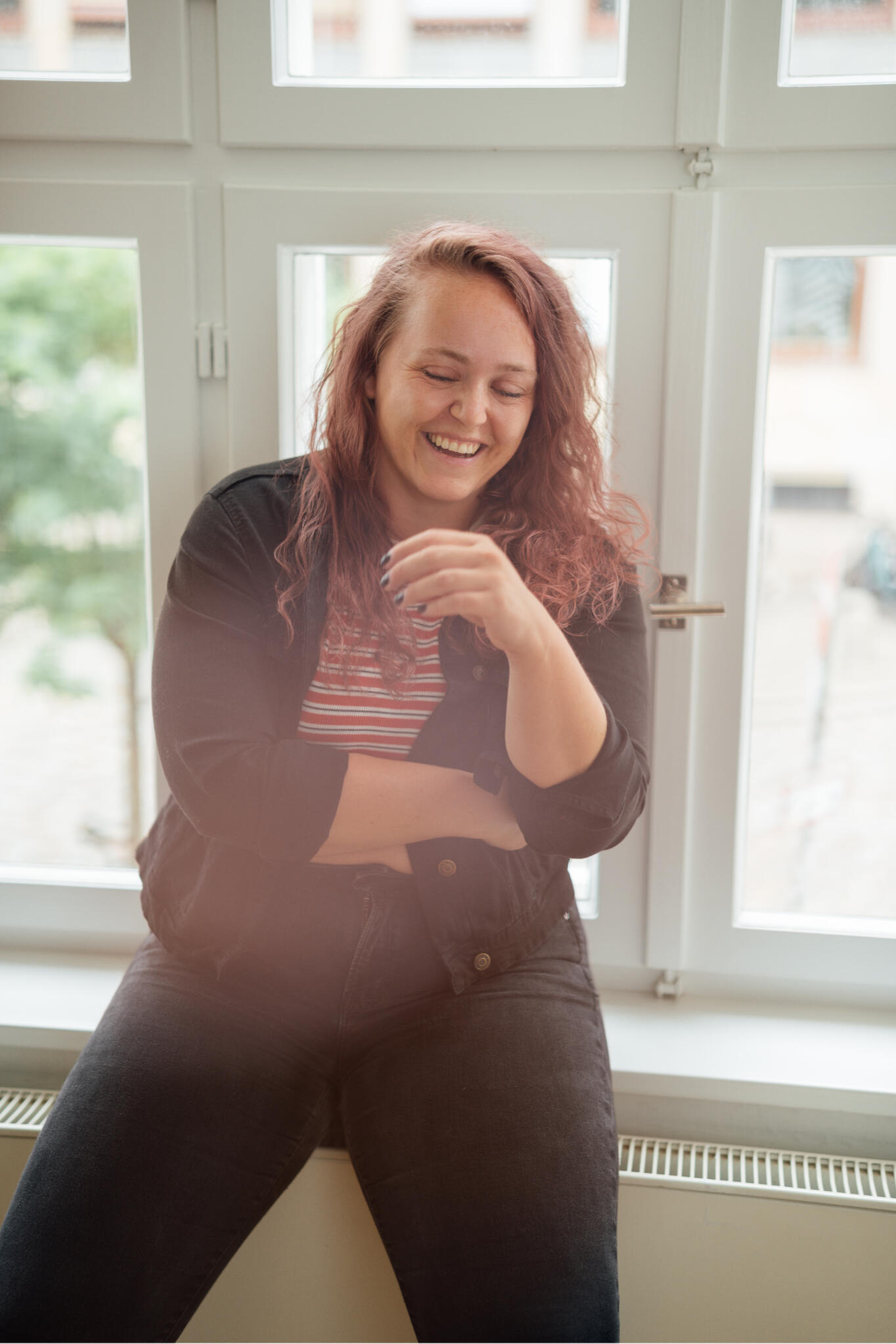 Rebecca – Feel Good Creator Rebecca sitzt auf einer Fensterbank und lacht